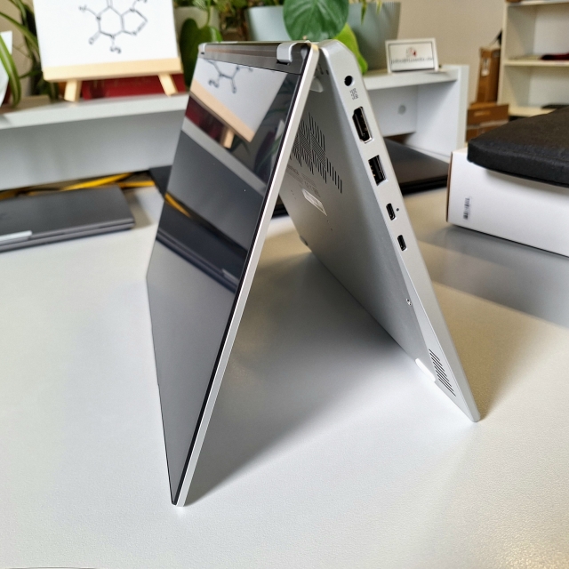 Ein Laptop ca. 270° geöffnet, steht wie eine Pyramide. Im Hintergrund unscharf Gegenstände auf einem Schreibtisch.