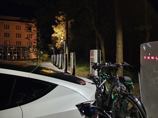 zu sehen ist im Vordergrund das Heck eines Teslas mit einem Fahrradträger auf dem Fahrradträger befinden sich zwei Fahrräder dahinter ist eine Reihe supercharger sichtbar