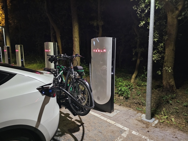 zu sehen ist das Heck eines Teslas mit einem Fahrradträger darauf befinden sich zwei Fahrräder dahinter vier supercharger Ladesäulen