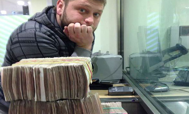 Roman Seleznev, in a photo released by the DOJ which shows him standing at an money exchange window with his head in his hand staring at the camera over several large piles of bundled cash.