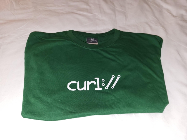 The picture shows a green t-shirt with the curl project logo in white color