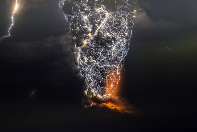 A dark sky fills most of this picture, centered on a massive column - resembling a tornado - of volcanic ash and fire surrounded by a web of lightning. Another lightning bolt is at the left-hand edge of the image. 