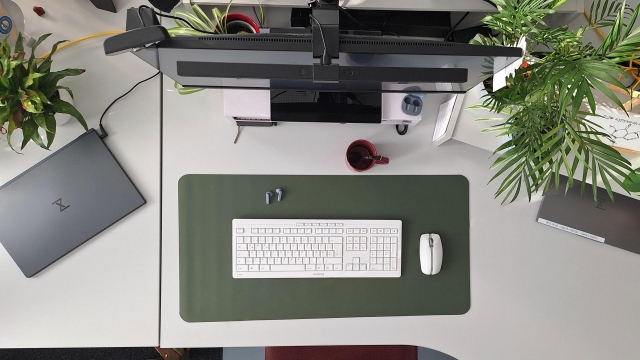 Blick von oben auf einen Schreibtisch. Man sieht eine grüne Deskmat, eine weiße Tastatur und Maus sowie Pflanzen und Notebooks.