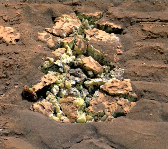 A broken rock is embedded in the red Martian ground. Yellow crystals were within the rock and are now visible on the surface. These crystals are elemental sulfur, a new discovery for Mars.